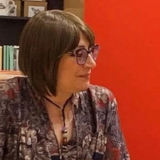 Fotografia di Angela Iannarelli: ritratto di tre quarti, occhiali dalla montatura chiara e camicetta a fantasia, seduta con il microfono in mano durante una presentazione in libreria