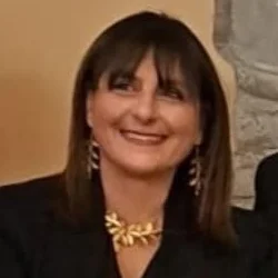 Fotografia di Anna Di Mauro: ritratto sorridente a mezzo busto, giacca scura e collana dorata