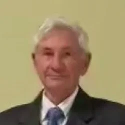 Fotografia di Cesare Pifano: ritratto frontale a mezzo busto, capelli bianchi, giacca scura e cravatta, su fondo giallo tenue