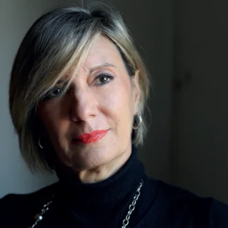 Fotografia di Donata Maria Biase: ritratto frontale in luce radente, dolcevita nero e collana a maglie larghe, su fondo scuro