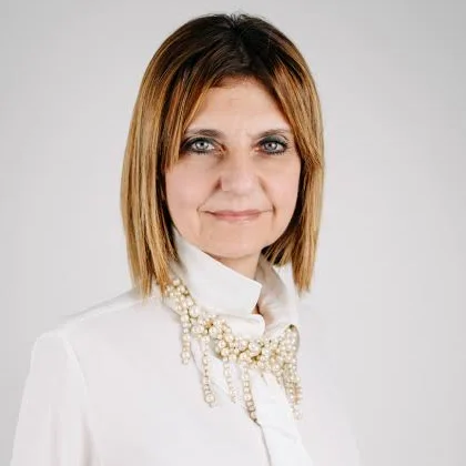 Fotografia di Monica Oriente: ritratto frontale in studio, camicia bianca con collana di perle, su fondo chiaro